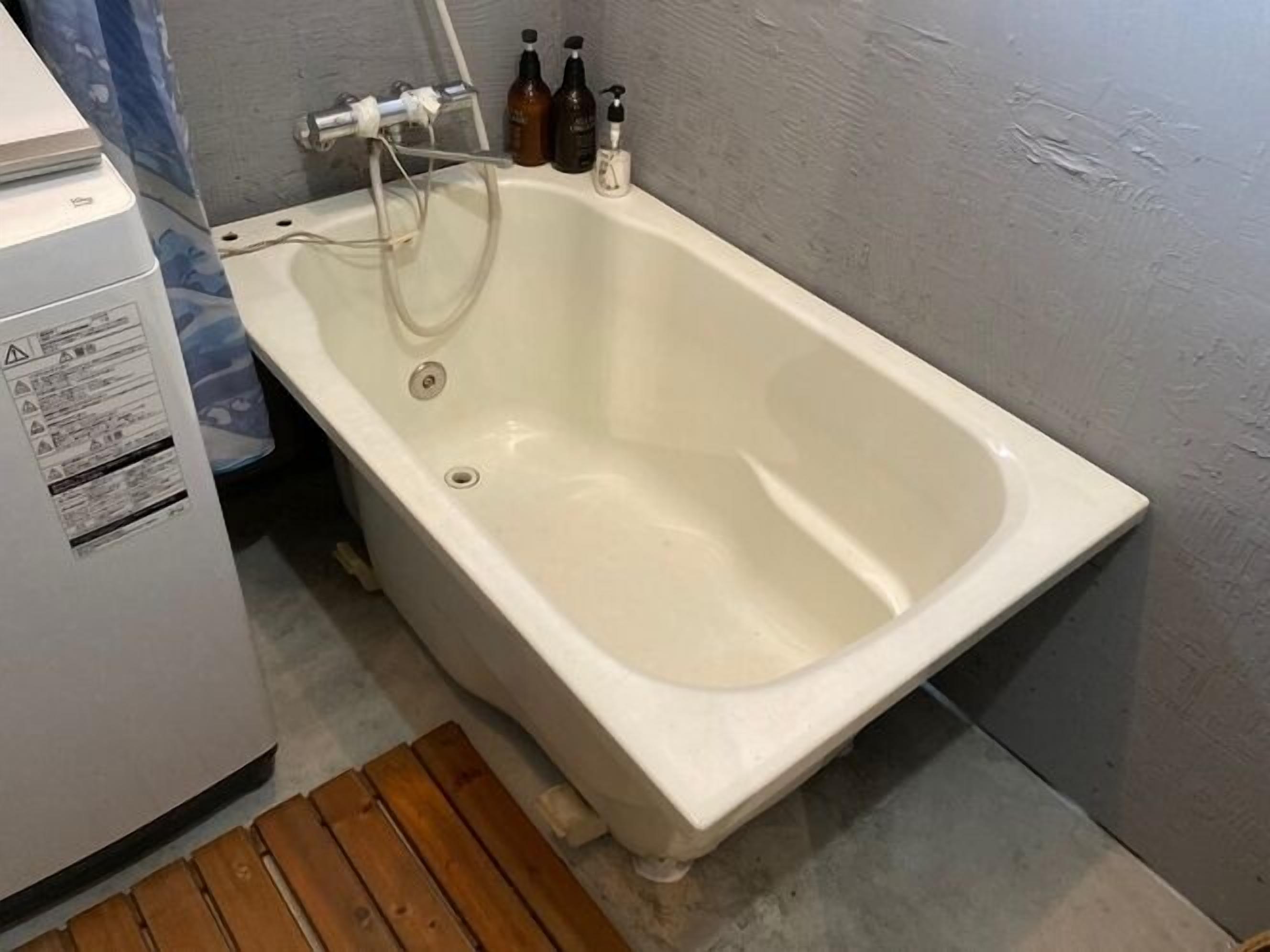 A white bathtub with a faucet and a drain, a wooden bench, and a wall-mounted heater.