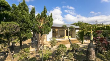 Una casa moderna con un porche cubierto, rodeada de varios árboles y plantas.