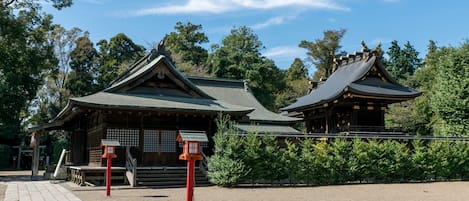 Un bâtiment japonais traditionnel, doté d’un toit en pente et d’une structure en bois, entouré de verdure.