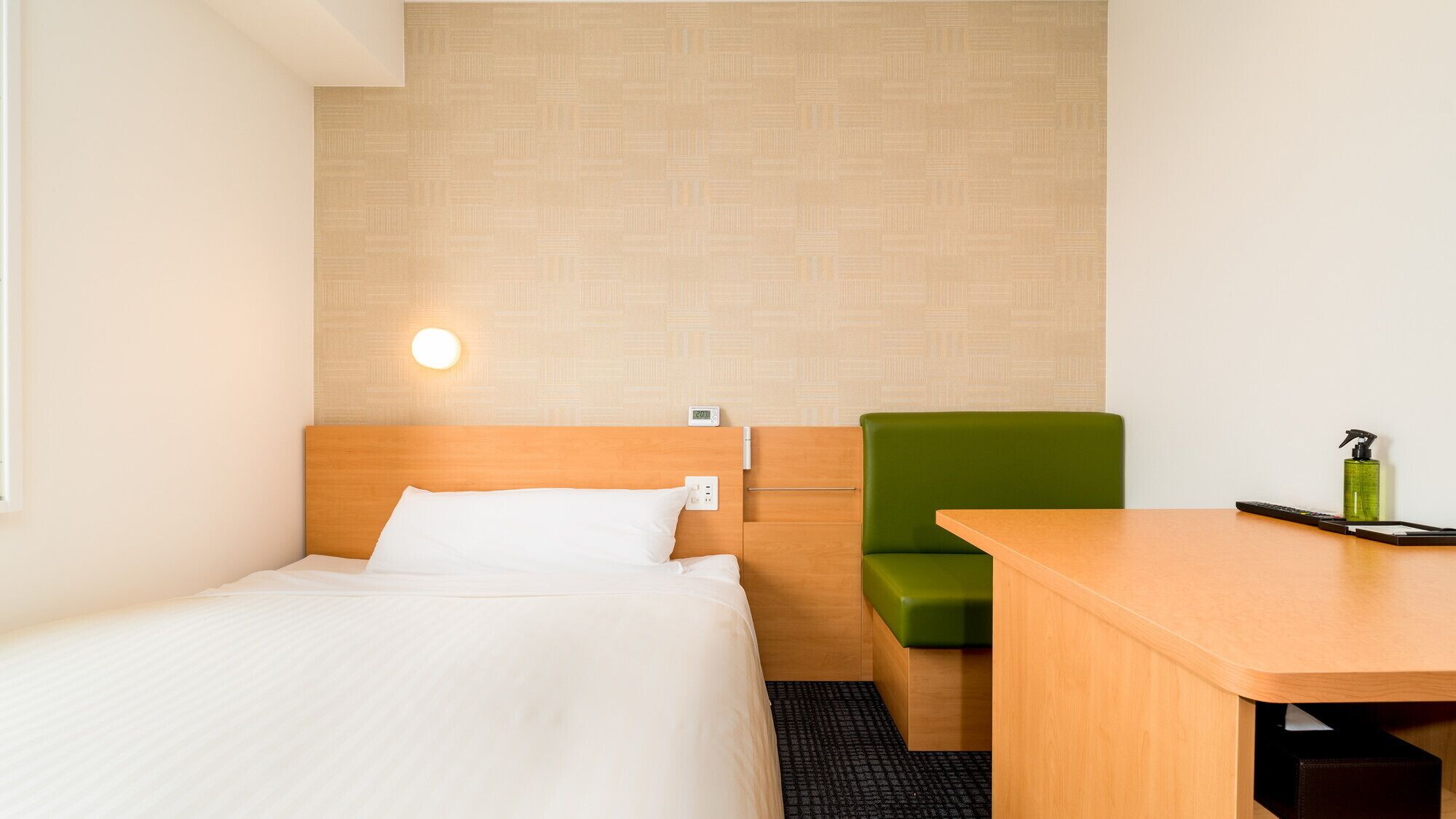 Een hotelkamer met een bed, een groene stoel, een houten bureau en een wandlamp.