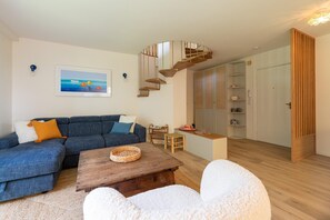 A modern living room with a blue sectional sofa, a wooden coffee table, and a staircase leading to a loft area. - Sea-View Duplex for Family (Villeneuve-Loubet)