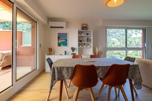 Un coin repas avec une table dressée pour quatre personnes, entourée de chaises, d’une bibliothèque et d’une fenêtre donnant sur un paysage verdoyant.