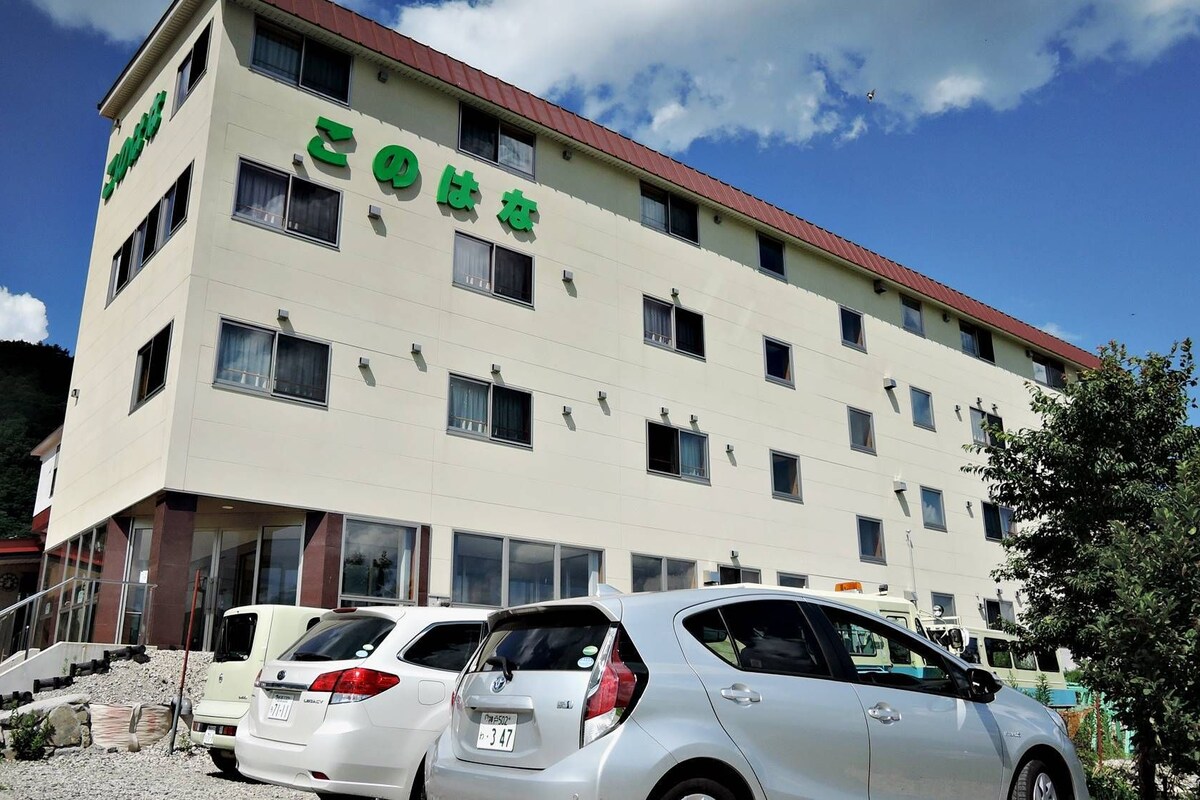 A multi-story hotel with a flat facade, several windows, and a parking area with cars.