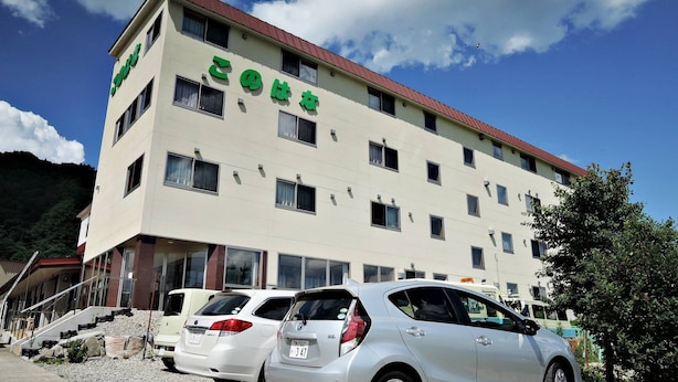 A multi-story building with a flat facade, several windows, and a parking area with cars. - Plateau Konohana (Yabu)