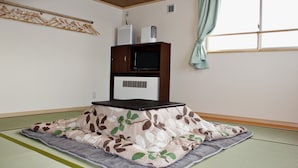 A room with tatami mats, a low wooden table, a television, and a heater. - Plateau Konohana (Yabu)