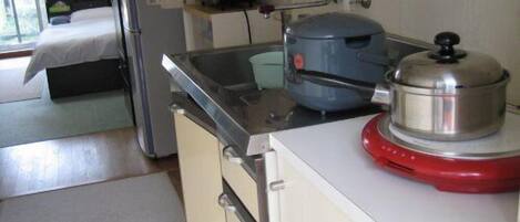 Una cocina compacta con un refrigerador, una tetera y una tetera roja eléctrica sobre la encimera.