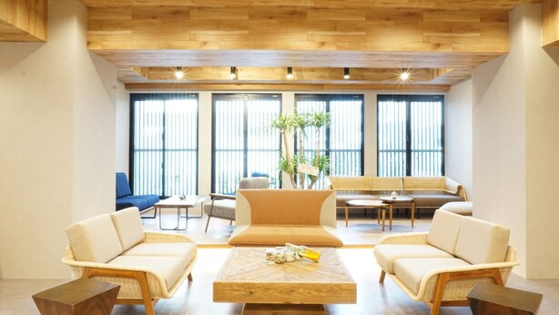 A modern lounge with a wooden ceiling, large windows, and comfortable seating areas. - Yukureba Maejima Hotel (Naha)