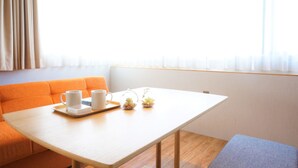 A room with a wooden table, a beige sofa, and a window with sheer curtains. - Yukureba Maejima Hotel (Naha)