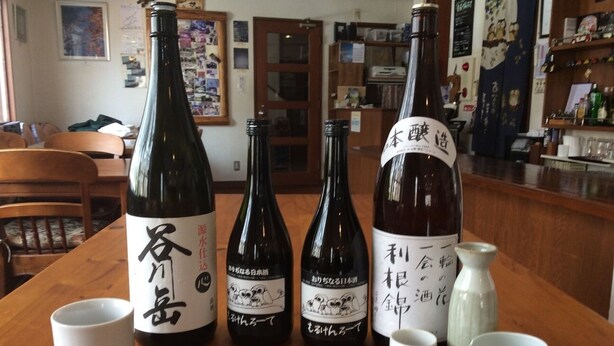Una mesa de madera con cuatro botellas de sake y varias tazas blancas pequeñas.