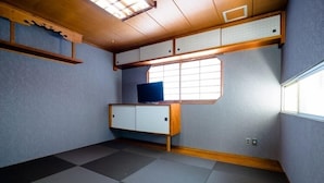 Habitación pequeña con suelo de tatami, un mueble bajo de madera, televisor y ventana con vistas.