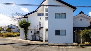 Un edificio residencial de dos pisos con fachada blanca, techo negro y una escalera visible que conduce al piso superior.