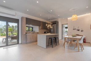 A modern kitchen with a central island, bar stools, and a dining area with a table and chairs. - Green & Purple, Apartment (Aegina)