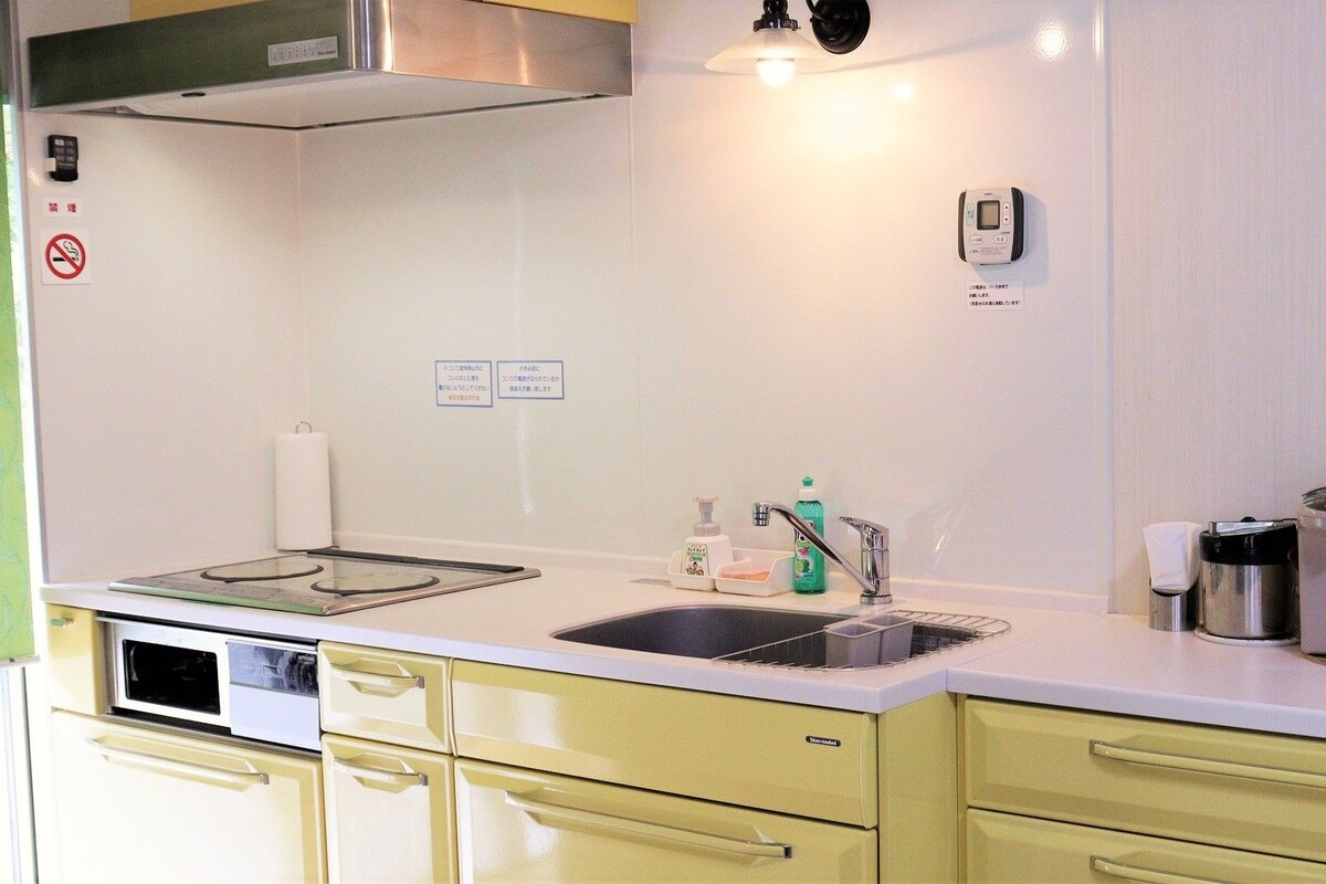 A compact kitchen with a stove, sink, and a coffee maker. There are cabinets and a microwave.