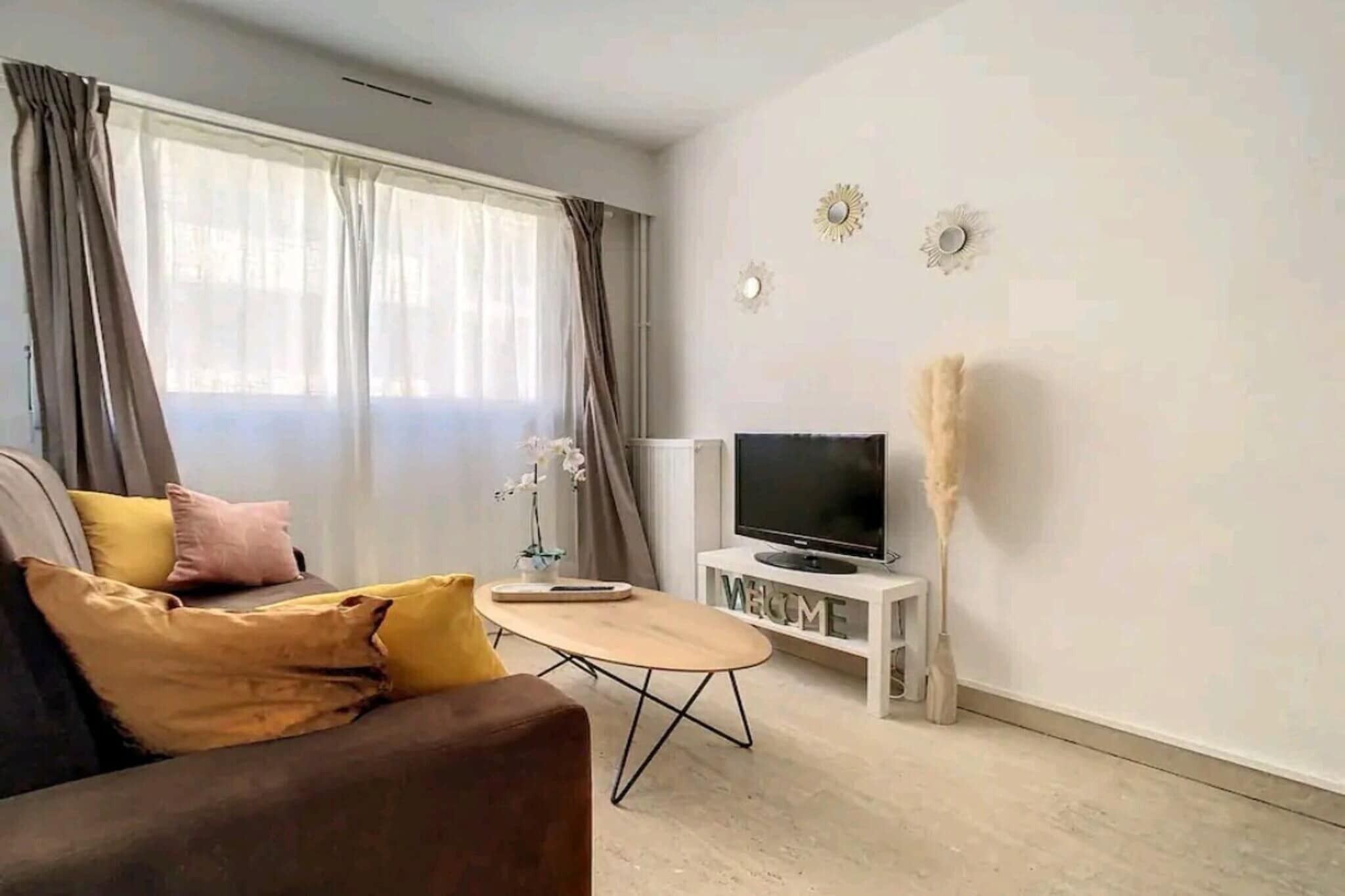 Een moderne woonkamer met een bank, een salontafel, een tv op een meubel en een raam met gordijnen.