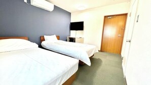 Ein Hotelzimmer mit zwei Einzelbetten, einem Flachbildfernseher, einem Schreibtisch und einer Tür.