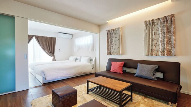 A modern bedroom with a large bed, a sofa, and a coffee table. - Condominium Yuyuki (Yomitan)