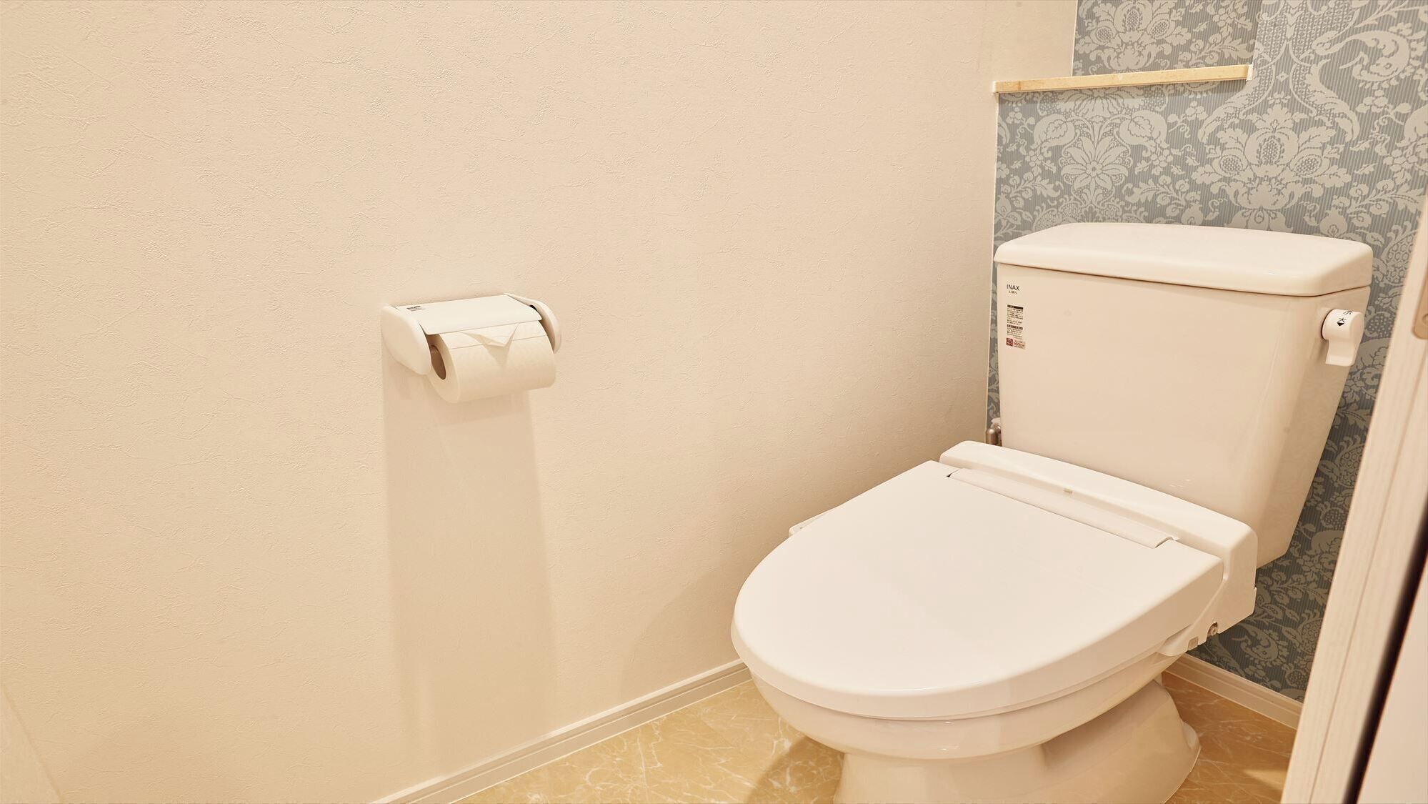 A toilet with a white lid and tank, a toilet paper holder on the wall, and a patterned wallpaper in the background.
