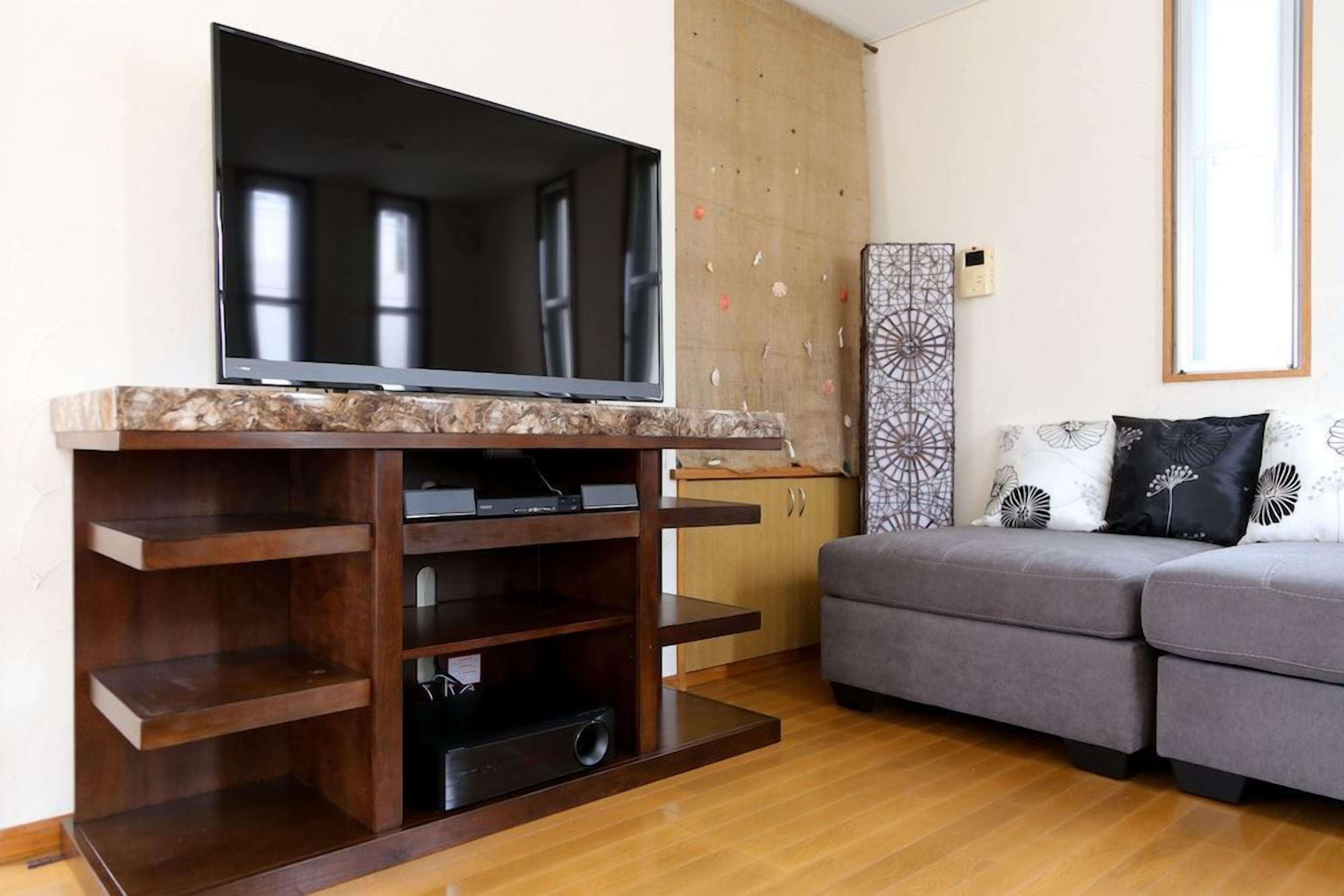 Ein Wohnzimmer mit einem Flachbildfernseher auf einem Holzboden, einem grauen Sofa und einer Anrichte.
