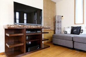 Un salon avec un téléviseur à écran plat posé sur un meuble en bois, un canapé gris et un buffet.
