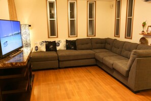 A living room with a sectional sofa, a flat-screen TV, and a decorative wall panel. - Palm Villa Ishigakijima Igusa (Ishigaki)