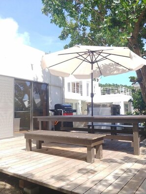 An outdoor deck with a wooden table and bench, a grill, and a large umbrella providing shade. - Palm Villa Ishigakijima Igusa (Ishigaki)
