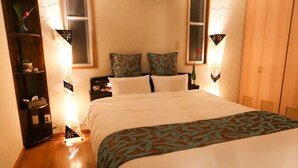 A neatly made bed with a patterned bedspread, a bedside table with a lamp, and a nightstand. - Palm Villa Ishigakijima Igusa (Ishigaki)