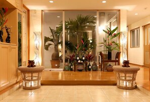 Un hall d’hôtel avec un comptoir d’accueil, des plantes en pot et des meubles en osier.