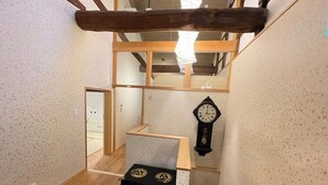 A compact room with a wooden floor, a black clock on the wall, and a small black chest. - Guesthouse Wazakura (Sakurai)
