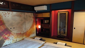 A hotel room with a bed, a wall with a decorative pattern, a small table with a lamp, and a framed picture. - Guesthouse Wazakura (Sakurai)