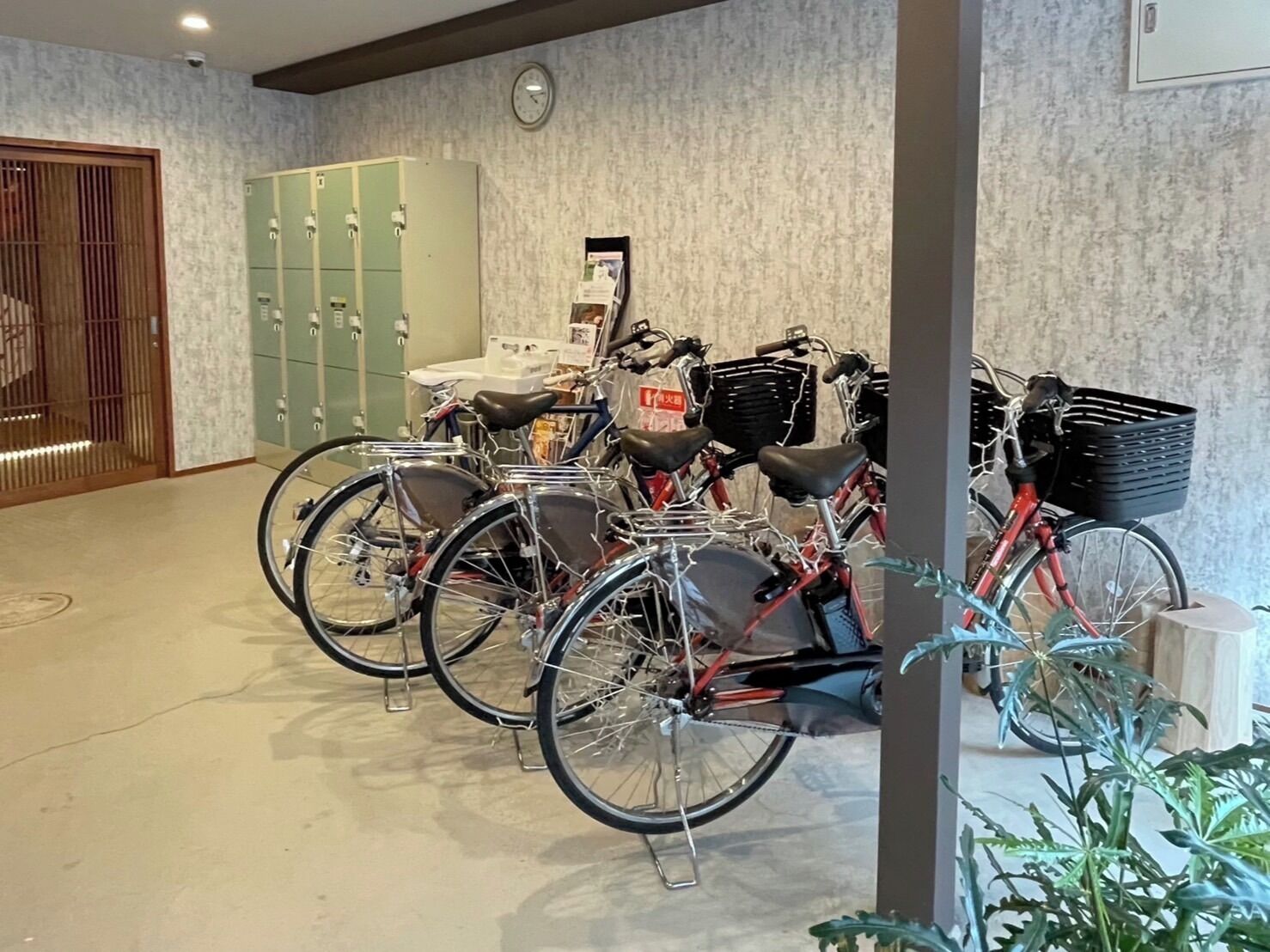 Una habitación con bicicletas apoyadas en una pared, un reloj y una serie de taquillas.