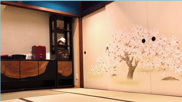 A traditional Japanese room with tatami flooring, a sliding door with cherry blossom painting, and a wooden cabinet with shelves. - Guesthouse Wazakura (Sakurai)