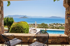 A patio with two chairs, a swimming pool, and a view of the sea and distant mountains.