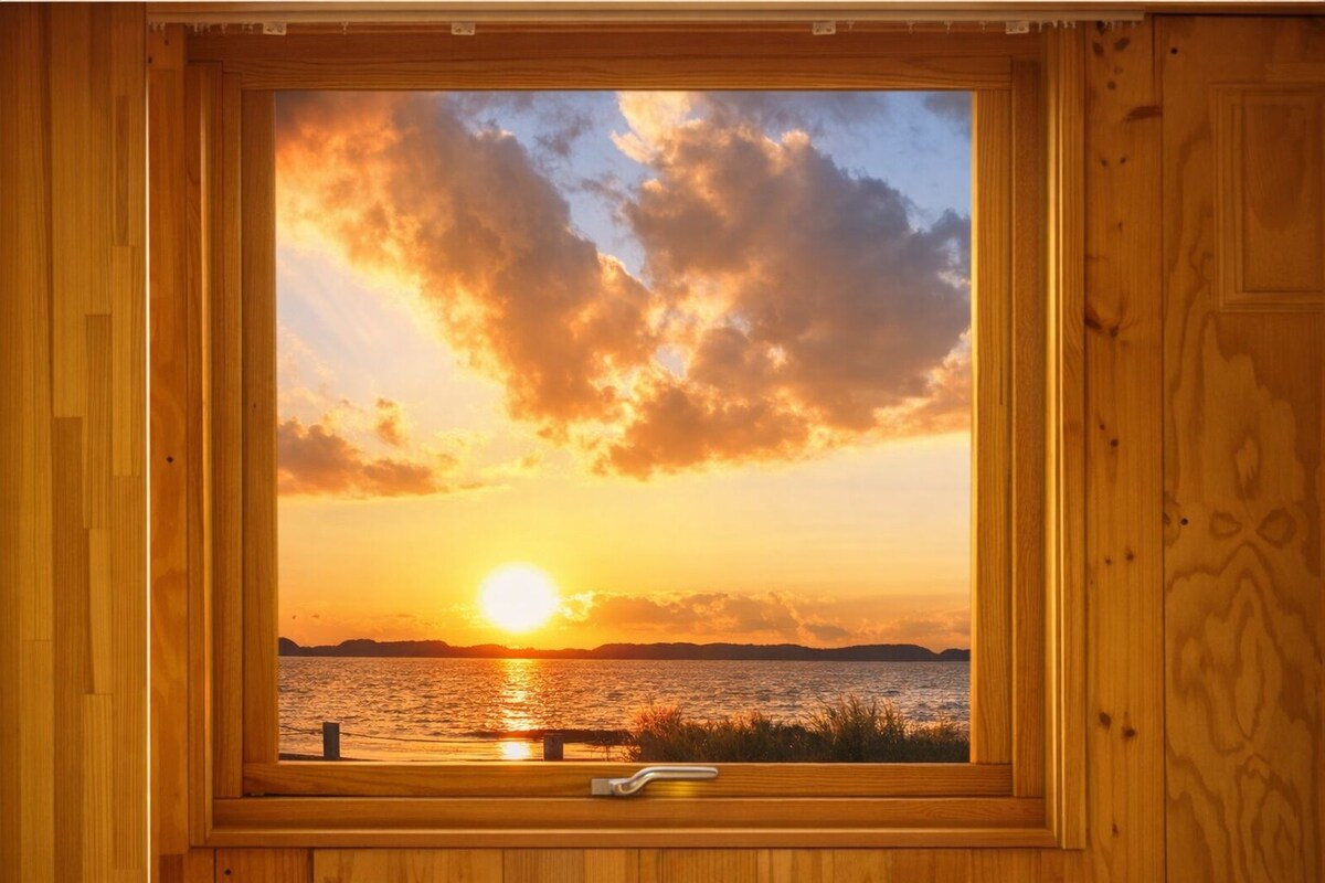 Ein Holzrahmenfenster mit Blick auf einen Sonnenuntergang über dem Wasser.