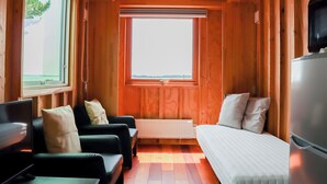 Ein gemütlicher Raum mit Holzwänden, einem großen Fenster, einem Bett, einer Couch und einem Fernseher.