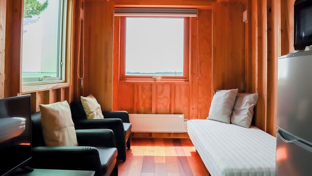 A compact room with wooden walls, a large window, a bed, a sofa, and a TV. - Kasumi Terrace Kasumigaura (Namegata)