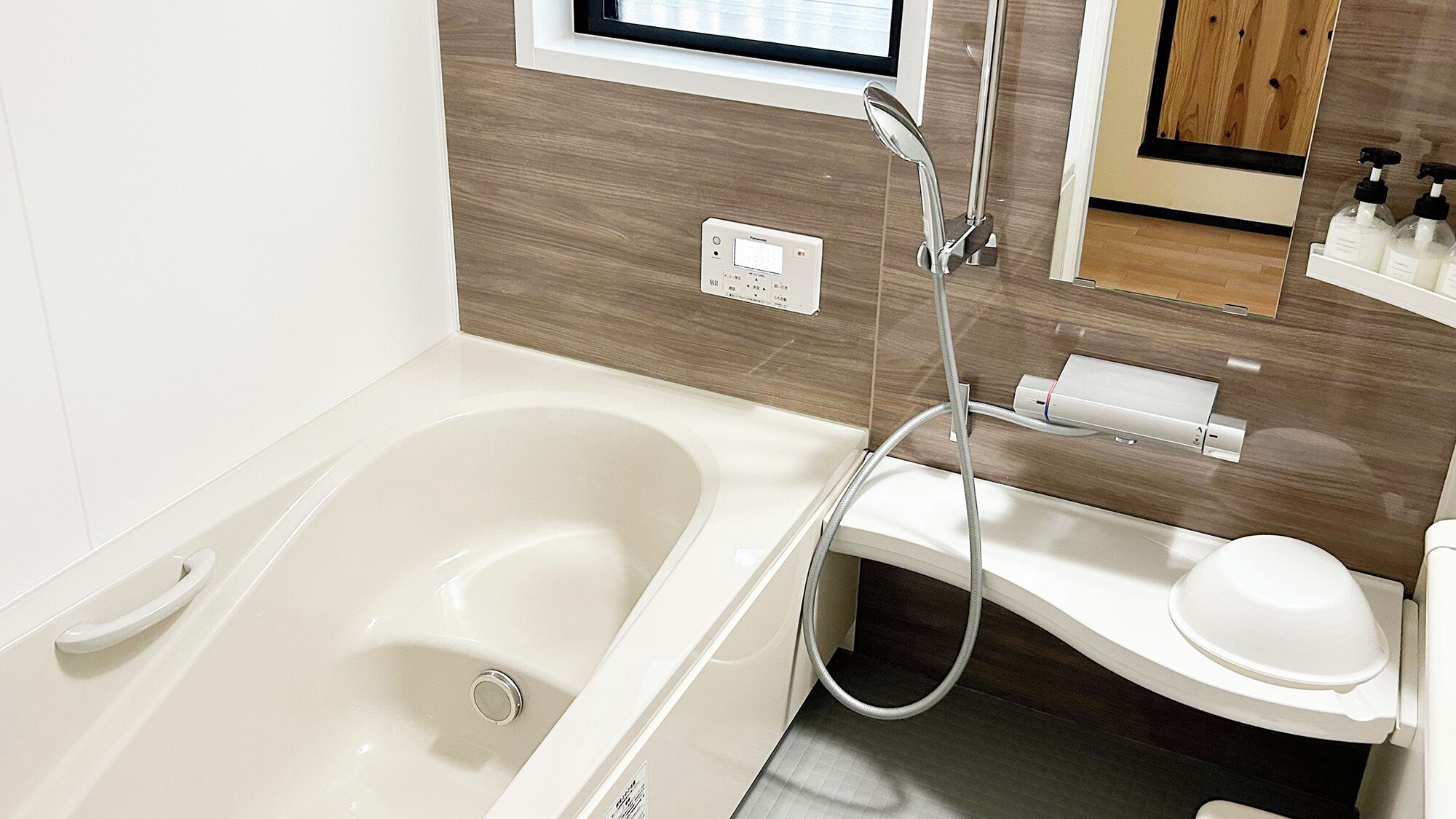 A modern bathroom with a bathtub, a toilet, a handheld showerhead, and a control panel.