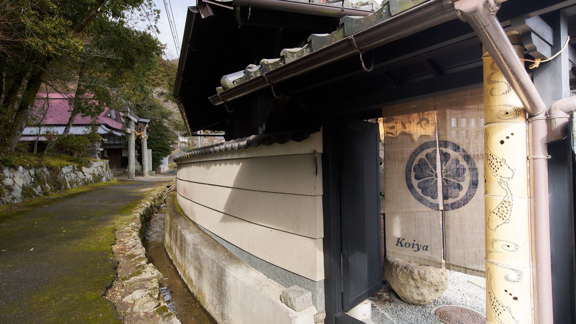 A traditional Japanese building with a curved wall, a wooden door with a circular design, and a stone pathway.