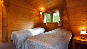 Una cabaña con dos camas, una ventana con cortinas y una lámpara en una mesita de noche.