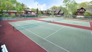 Una cancha de tenis con una red, rodeada de edificios y árboles.