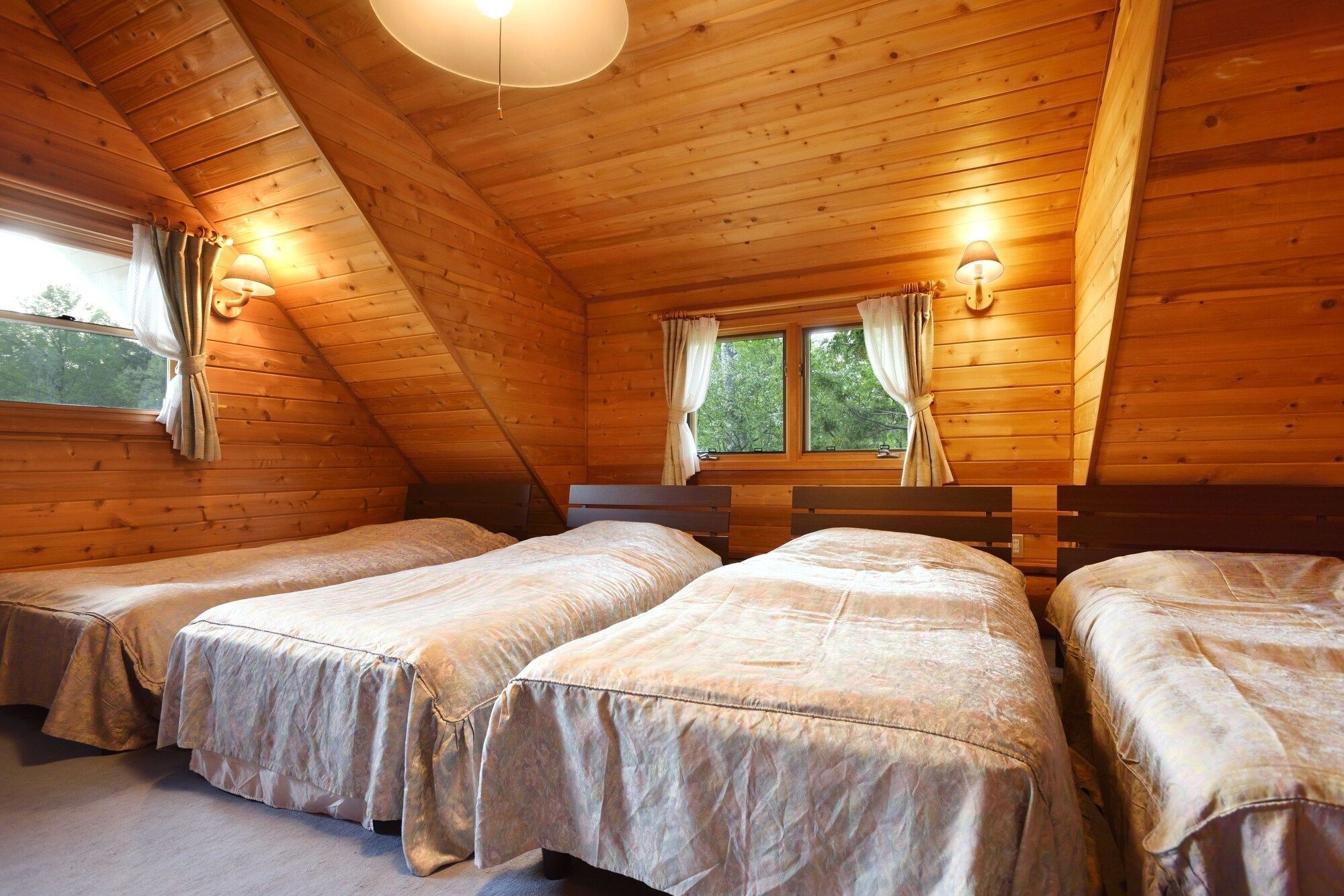Een kamer met houten wanden en schuine plafonds, met twee bedden met identiek beddengoed en een raam met gordijnen.