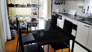 Una cocina funcional con una mesa negra, armarios blancos y un lavavajillas. Hay ollas y sartenes en las estanterías, y una tetera sobre la encimera.
