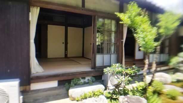 Una habitación tradicional japonesa con suelo de tatami, puertas correderas y un pequeño jardín con plantas y un farol de piedra.