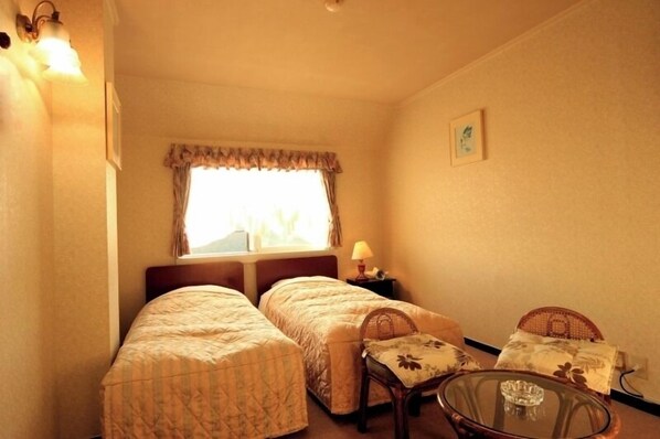 A small, cozy room with two single beds, a small table, and a chair.