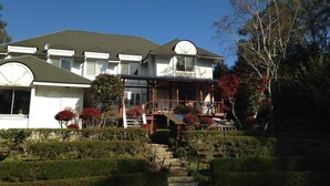 A two-story house with a balcony, surrounded by well-maintained hedges and a small garden.