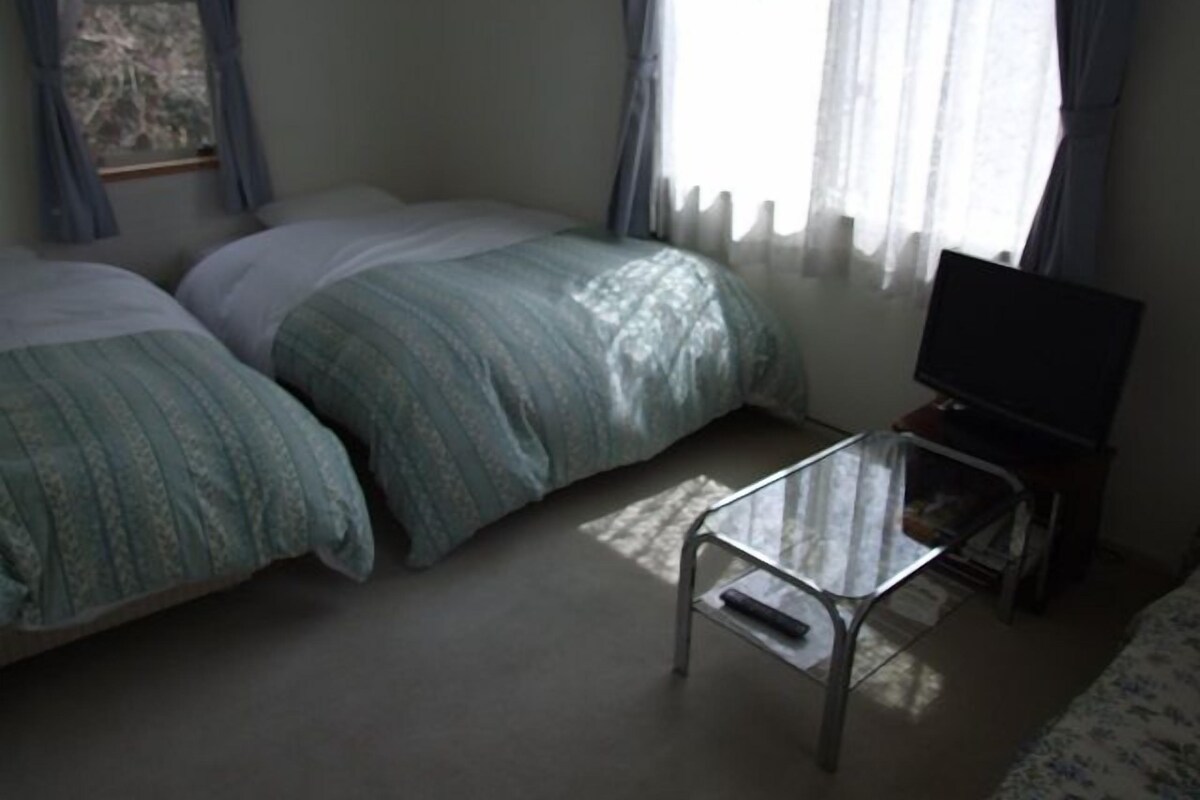 Un dormitorio con dos camas, un televisor sobre un soporte y una ventana con cortinas.