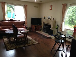 A living room with a leather sofa, a glass coffee table, a TV, a fireplace, and a view of greenery outside.