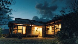 A rustic wooden house with large windows and a porch, surrounded by natural landscape.