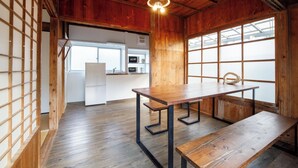 A wooden interior with a dining table, benches, and a kitchen area visible through a large window.