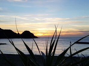 A coastal sunset with silhouettes of mountains and vegetation in the foreground. - House Hotel Amami Minpaku Mura & Sauna (Amami)