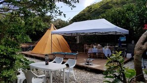 A tented outdoor dining area with tables and chairs, surrounded by greenery. - House Hotel Amami Minpaku Mura & Sauna (Amami)